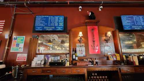 Interior of a bar featuring a wooden counter, screens displaying menus, and a decorative bear on the wall.