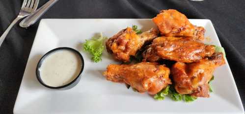 A plate of crispy chicken wings with a side of ranch dressing on a bed of lettuce.