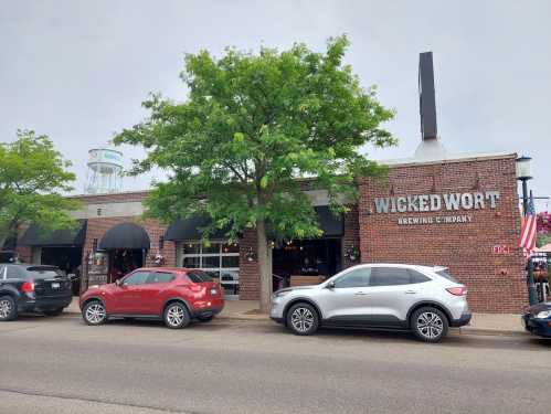 Exterior of Wicked Wort Brewing Company, featuring a brick facade, large windows, and parked cars in front.