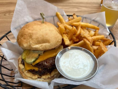 A juicy cheeseburger with pickles and a side of crispy fries, served with a small bowl of dipping sauce.