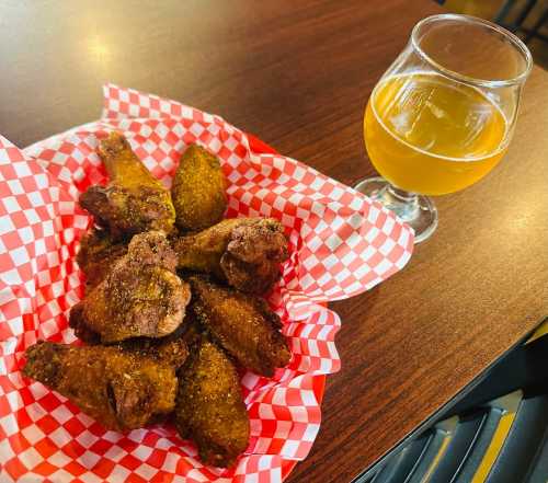 A basket of seasoned chicken wings with a glass of golden beverage on a wooden table.