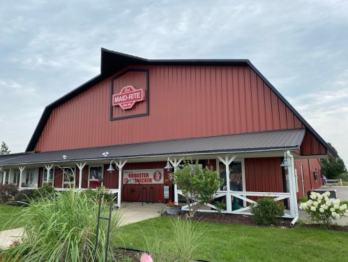 Red barn-style restaurant with a sign reading "Maid-Rite" and a grassy area in front. Overcast sky above.