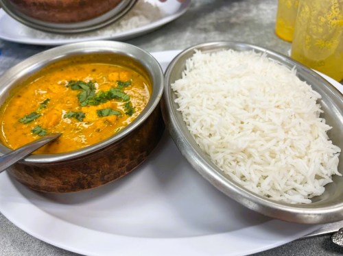 A bowl of curry with chicken and herbs next to a serving of fluffy white rice on a plate.
