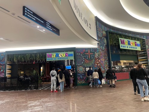 Entrance of Marcus Bar & Grill, featuring colorful signage and a crowd of people waiting outside.