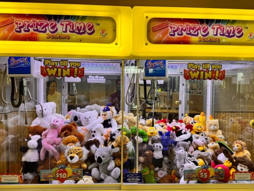 Two claw machines filled with colorful stuffed animals, labeled "Prize Time," with signs indicating play costs.