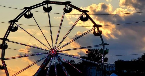 A silhouetted Ferris wheel against a colorful sunset with clouds in the background.