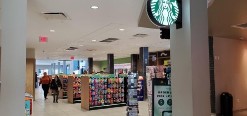 Interior of a shopping area featuring a Starbucks, snack displays, and shoppers walking through the space.
