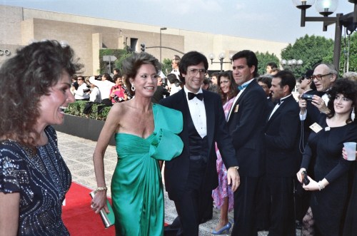 A glamorous group at a red carpet event, featuring a woman in a green dress and a man in a tuxedo, smiling and posing.
