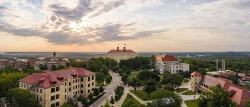 A panoramic view of a university campus at sunset, featuring historic buildings and lush greenery under a cloudy sky.