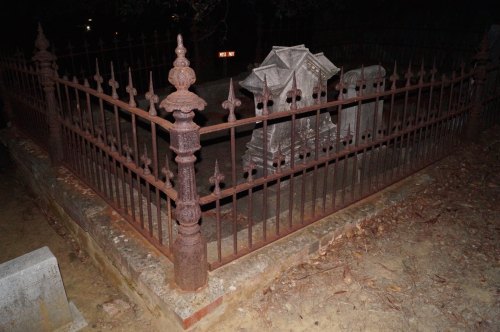 A rusted iron fence surrounds an old, weathered grave in a dimly lit cemetery.