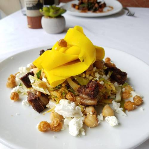 A colorful dish featuring shredded vegetables, beef, mango, and cheese, garnished with crispy toppings on a white plate.