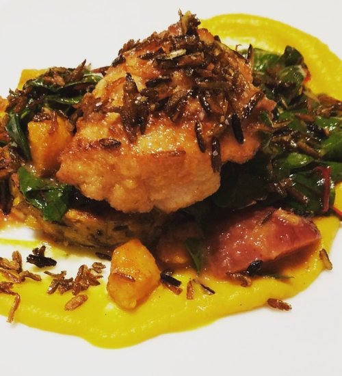 A beautifully plated dish featuring crispy fried topping, greens, and a vibrant yellow puree on a white plate.