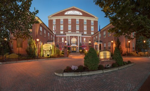 Historic brick building with columns, surrounded by greenery and lights, at dusk. Entrance features a welcoming sign.