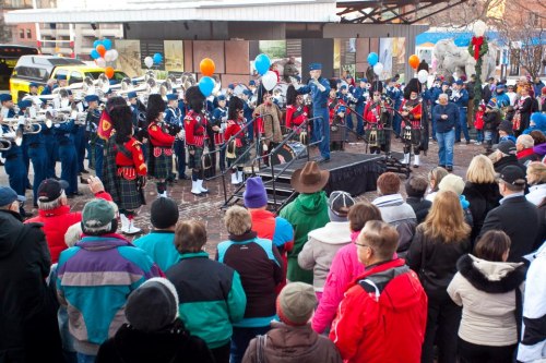 A crowd watches a performance by a marching band and bagpipers at an outdoor event, with colorful balloons in the background.