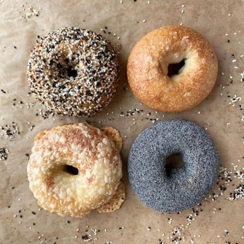 Four bagels on parchment paper: one with sesame seeds, one plain, one with poppy seeds, and one with a crispy crust.
