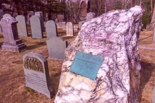 A colorful marble gravestone in a cemetery, surrounded by traditional headstones and trees in the background.