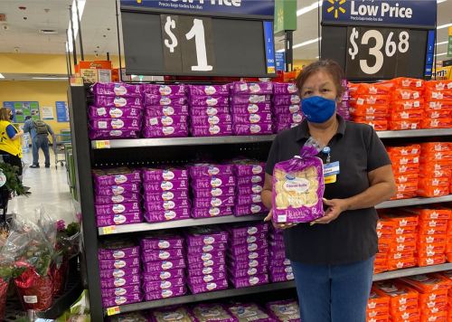 A woman in a mask holds a package of cookies in a store aisle with colorful product displays behind her.