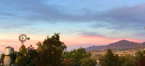 A scenic view of a sunset with mountains, trees, and a windmill against a colorful sky.
