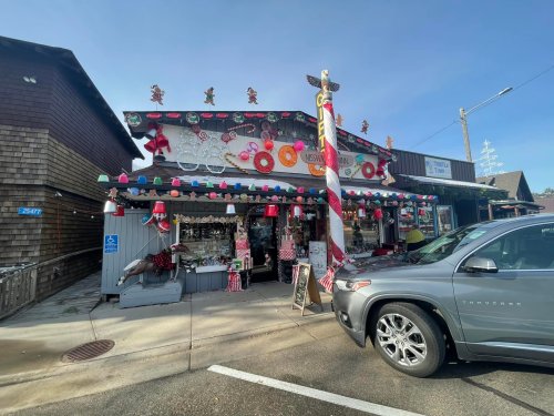 A festive shop decorated with holiday ornaments and lights, featuring a horse statue outside and a parked gray car.