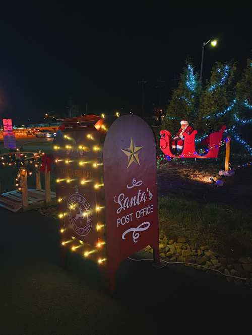 A festive mailbox labeled "Santa's Post Office" adorned with lights, next to a decorated Christmas tree and sleigh.