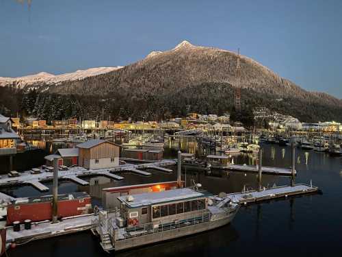 A serene harbor at dusk, with snow-covered mountains and boats docked in a calm waterway.