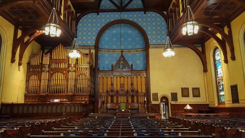 Interior of a church featuring a large organ, stained glass windows, and a beautifully painted ceiling.