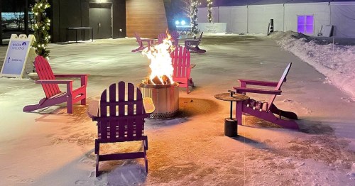 A cozy outdoor scene with purple chairs around a fire pit on a snowy surface, illuminated by soft lights.