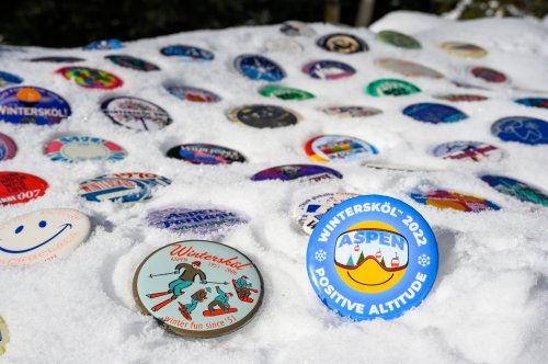 A snowy surface covered with colorful badges, featuring designs and text related to the Wintersköl event in Aspen.