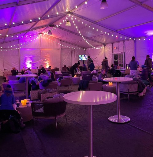 A cozy tented space with soft lighting, seating areas, and people socializing.