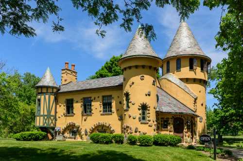 A whimsical castle-like building with turrets, stone accents, and a sign reading "OPEN," surrounded by greenery.