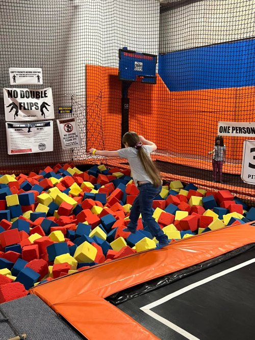 A child plays on a trampoline, surrounded by colorful foam blocks in a fun indoor activity center.