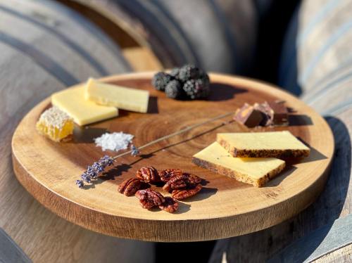 A wooden platter with assorted cheeses, nuts, honeycomb, chocolate, and blackberries, set against wine barrels.