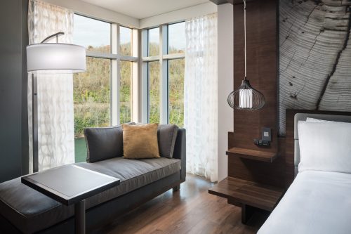 Modern hotel room featuring a cozy sofa, large windows, and stylish lighting with a view of nature outside.