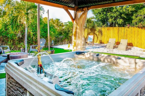 A hot tub with bubbling water under a gazebo, surrounded by palm trees and lounge chairs in a tropical setting.
