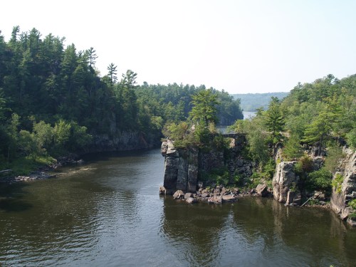 A serene river winding through lush green forests and rocky cliffs under a clear blue sky.