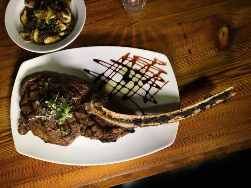 A large, grilled tomahawk steak garnished with herbs, served on a white plate with a drizzle of sauce.