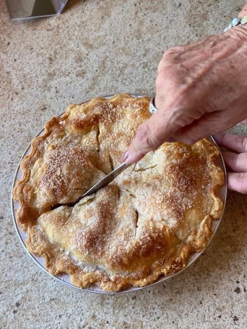 A hand cutting into a freshly baked apple pie with a golden crust and sugar topping.
