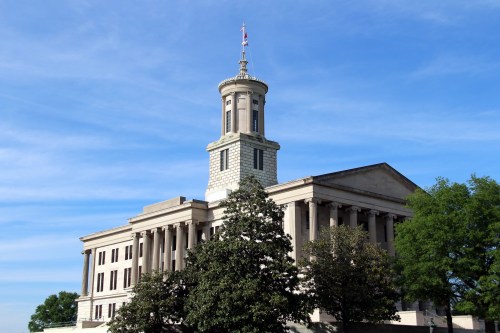 Historic building with a tall tower, surrounded by trees and a clear blue sky.
