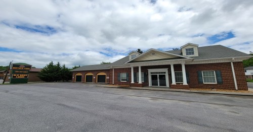 A brick building with a gray roof and large windows, featuring a sign for "Big Bass Lodge" in a cloudy sky.