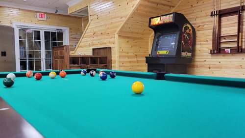A pool table with colorful balls and a vintage arcade game in a wooden-paneled room.