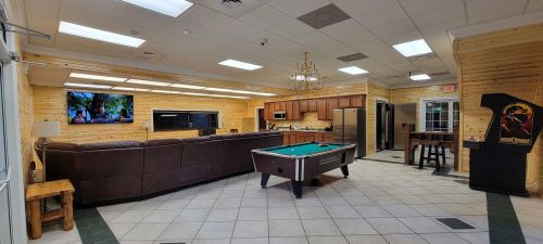 A spacious lounge with a pool table, large TV, kitchen area, and wooden decor, featuring comfortable seating.