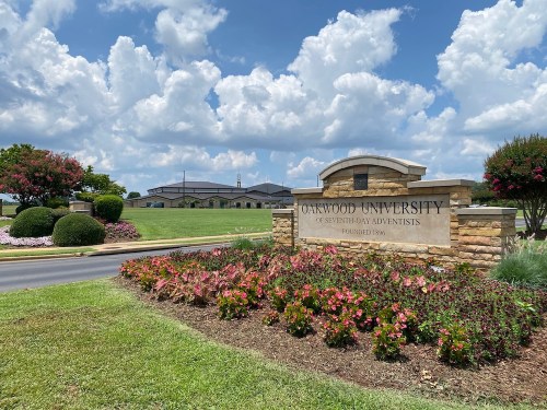 Sign for Oakwood University with landscaped gardens and a blue sky filled with clouds in the background.