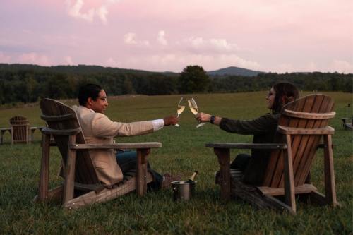 A couple toasts with champagne in outdoor chairs, surrounded by a scenic landscape at sunset.