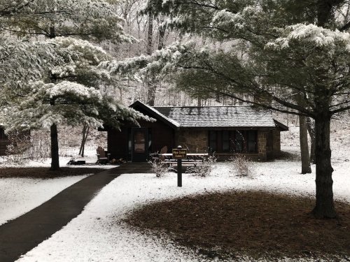 A cozy cabin surrounded by snow-covered trees and a path leading to the entrance.