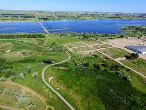 Aerial view of a lush landscape featuring a winding road, green fields, and a large body of water in the background.