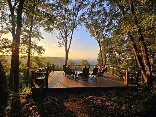 A wooden deck surrounded by trees, with people sitting and enjoying a sunset view over the mountains.