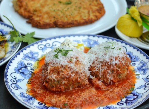 Two meatballs topped with cheese in a rich tomato sauce, served on a decorative plate with garnishes.