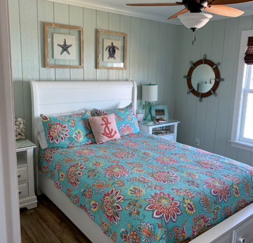 Brightly decorated bedroom with a white bed, colorful floral quilt, and nautical-themed decor on light green walls.