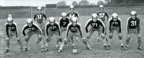 A vintage black-and-white photo of a football team lined up in formation on a grassy field.