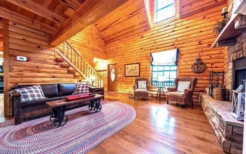 Cozy log cabin living room with wooden walls, a fireplace, and comfortable seating. Bright natural light from windows.
